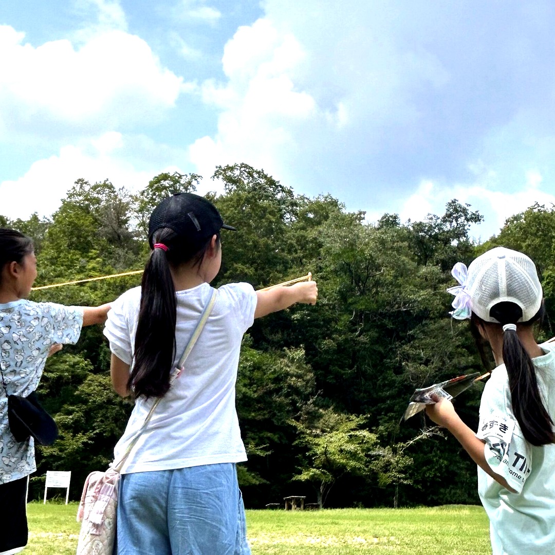 自然の中で紙ひこうきを飛ばす子どもたち
