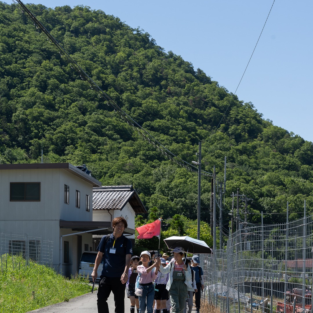 スタッフに続いて里山の農道を歩く子どもたちの列