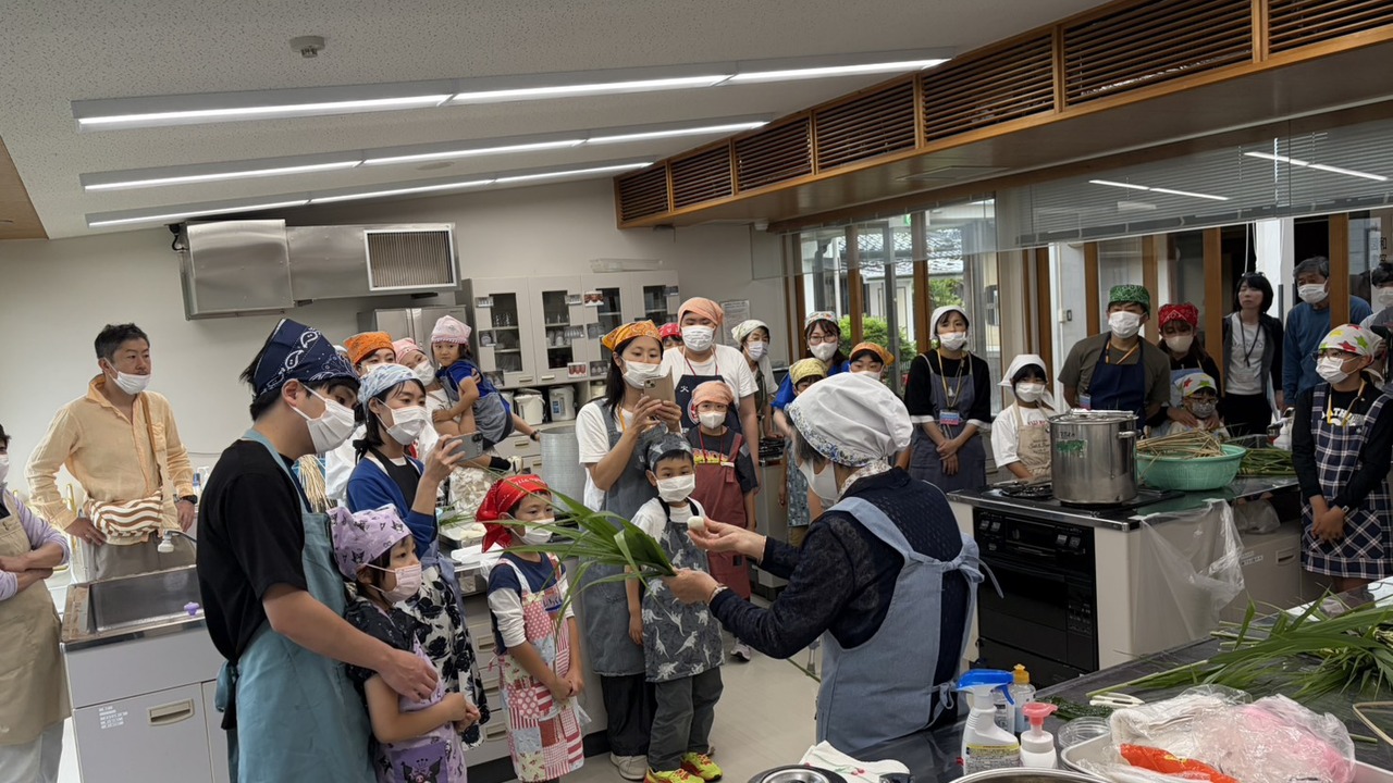 ちまき作り体験会の会場で嶋田さんの実演を囲む親子連れの参加者たち