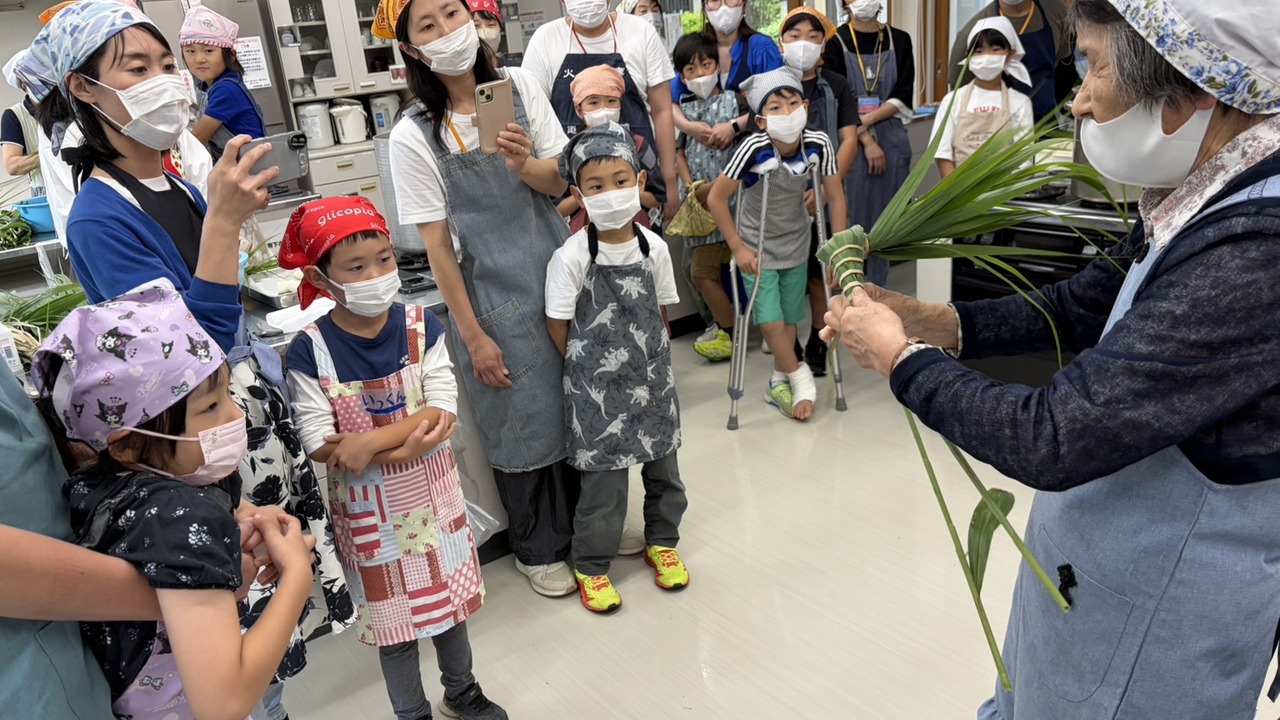 91歳の嶋田さんがちまきの巻き方を実演し、子どもや保護者が見入る様子