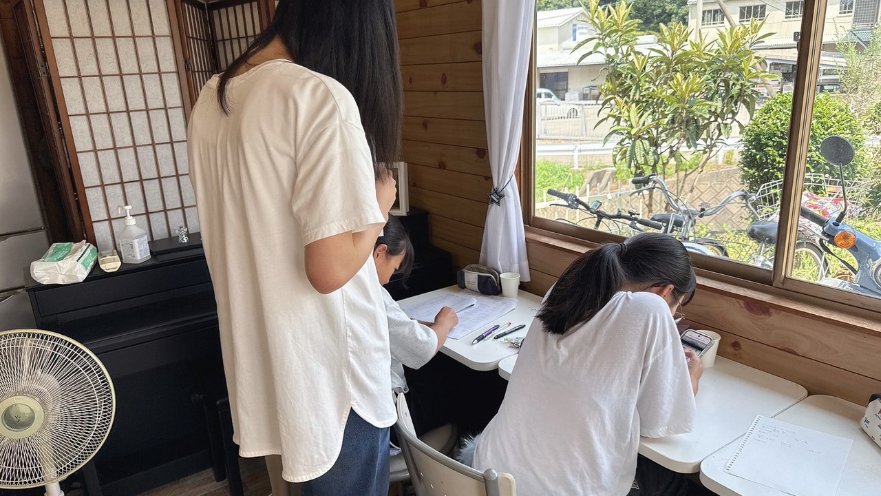 窓辺の机で子どもの手元をのぞき込みながら教えるスタッフ