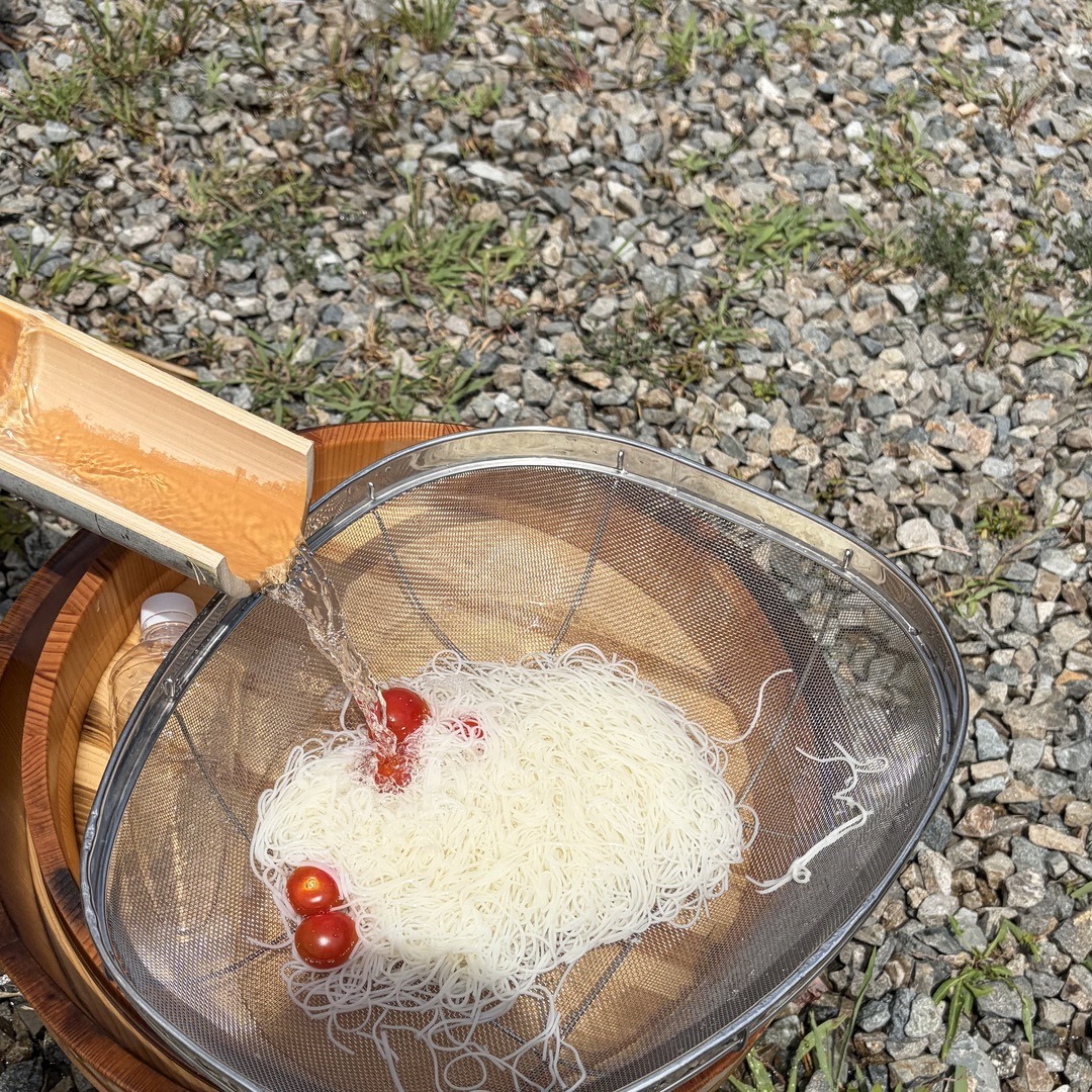 竹の樋の先で受け止められたそうめんとミニトマト