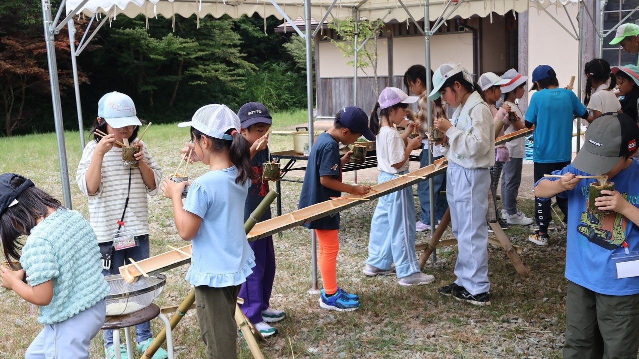 竹の樋に並んで流しそうめんをすくう子どもたち