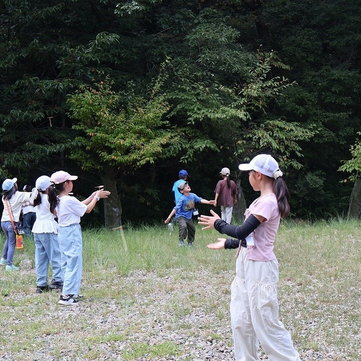 広場で竹とんぼを空高く飛ばす子どもたち