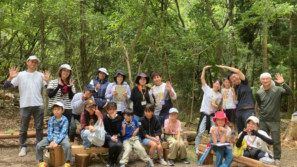 宝の森の広場で手を振る参加者と地元スタッフの集合写真