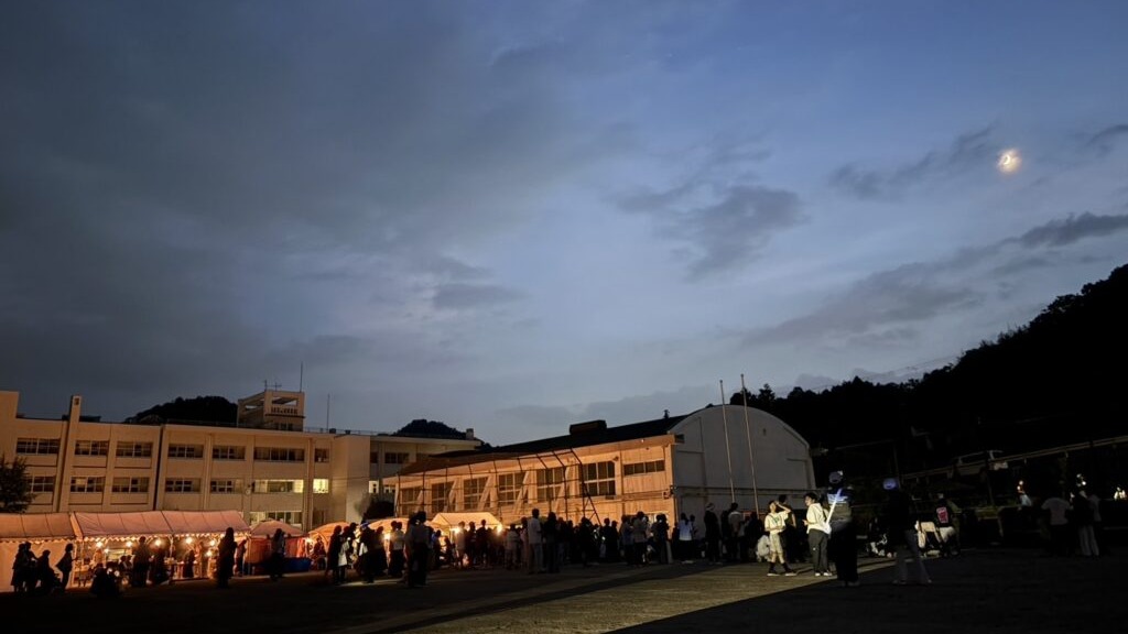 夕暮れの西谷小学校グラウンドに集まる第40回西谷ふるさとまつりの来場者