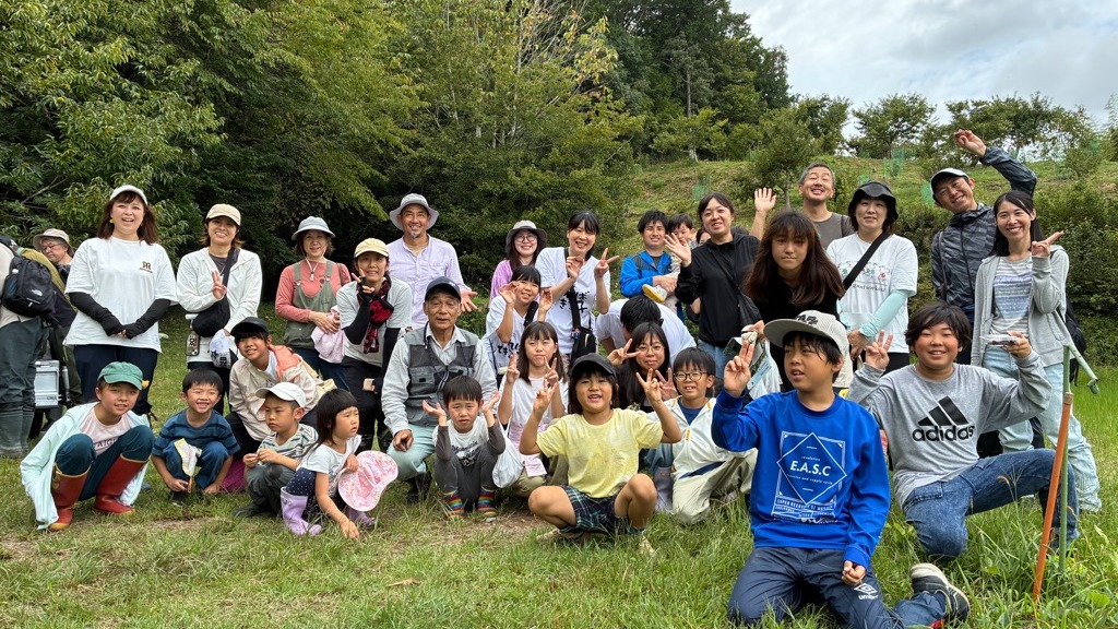 栗園の草地に並んだ参加者と栗園再生プロジェクトメンバーの集合写真